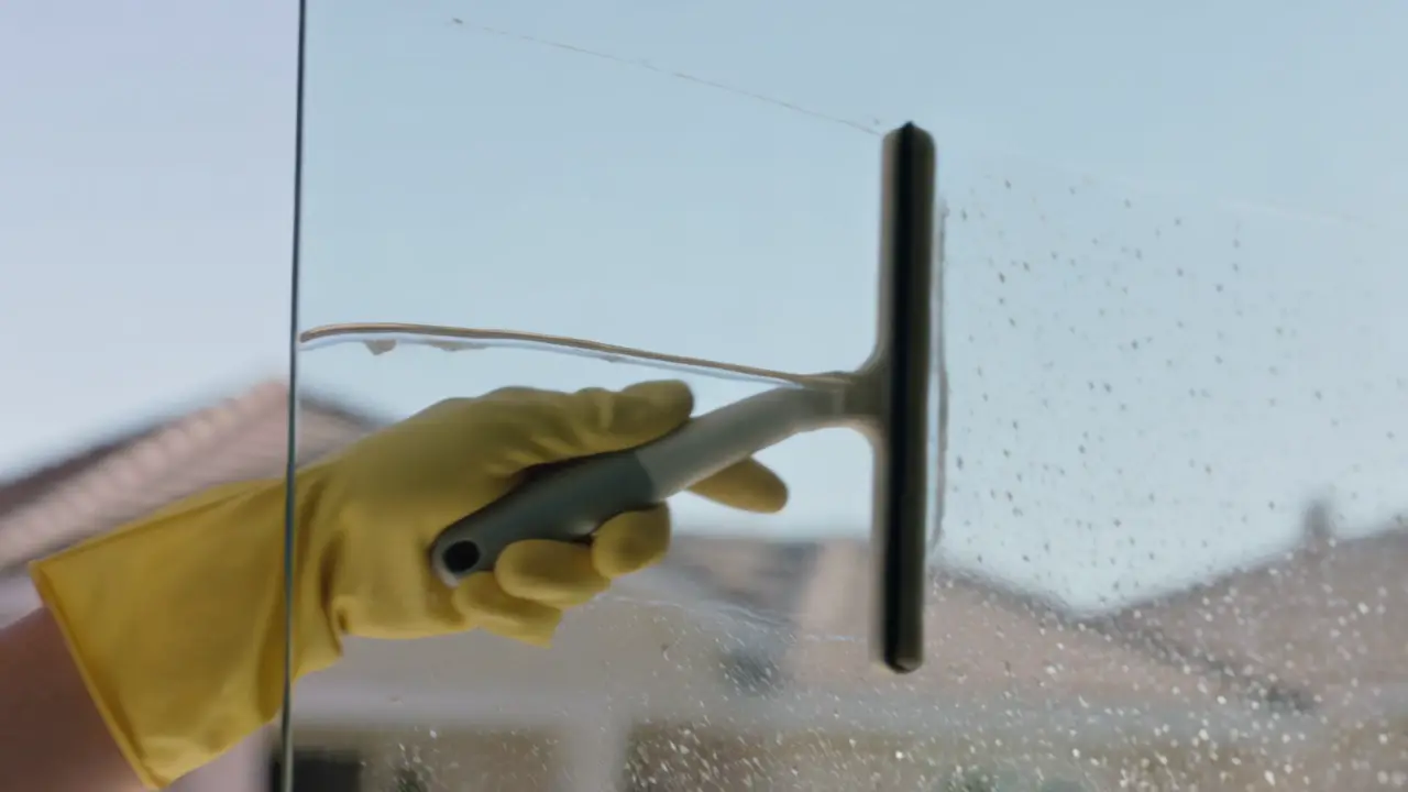 Close view of a squeegee pulling a clean sheet of water down a large pane.